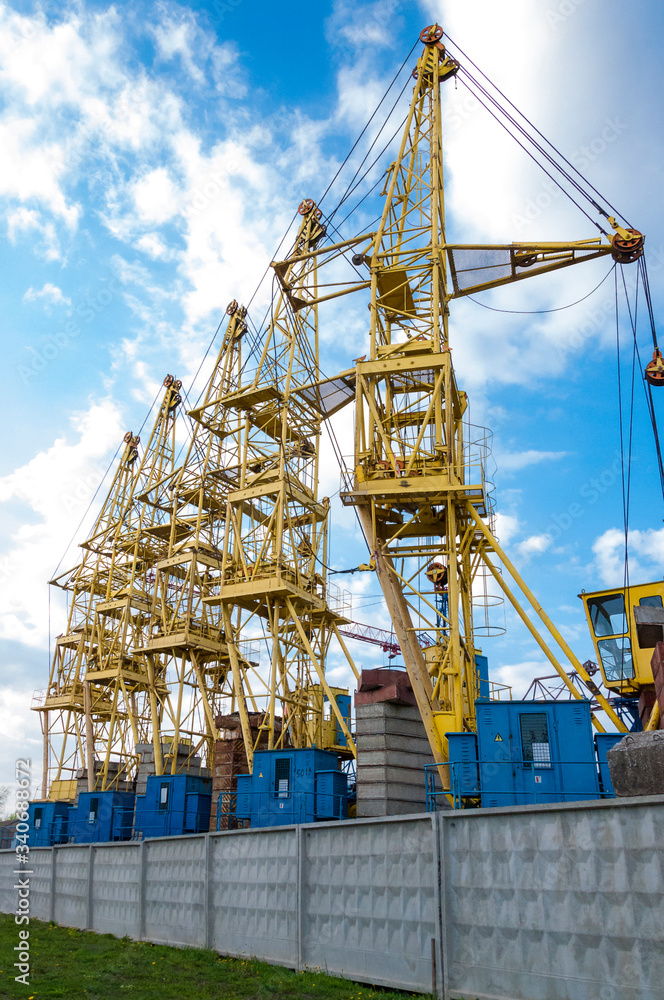 Yellow cranes parked behind a concrete fence. Broken iron cranes in the parking lot. Yellow cranes parked behind a concrete fence. Broken iron cranes in the parking lot.