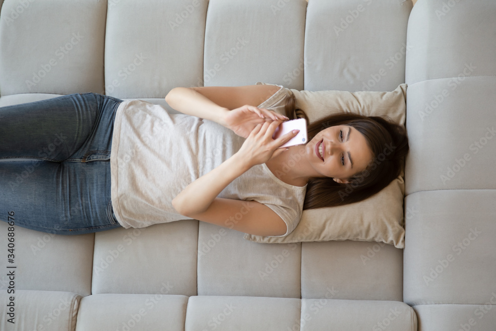 Obraz premium Top view happy attractive young woman using smartphone lying on sofa and getting good news. Relaxing young student user using mobile modern technology for online social chat and shopping.