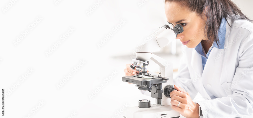 A female laboratory researcher looks into a microscope covering right half of the picture A female laboratory researcher looks into a microscope covering right half of the picture