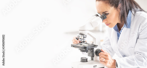 A female laboratory researcher looks into a microscope covering right half of the picture