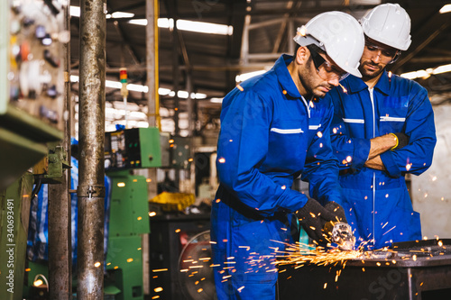 Group of technician industrial engineers wearing safety uniform and safety helmet cutting metal part using hand angle grinder machine. Large industrial factory background. photo