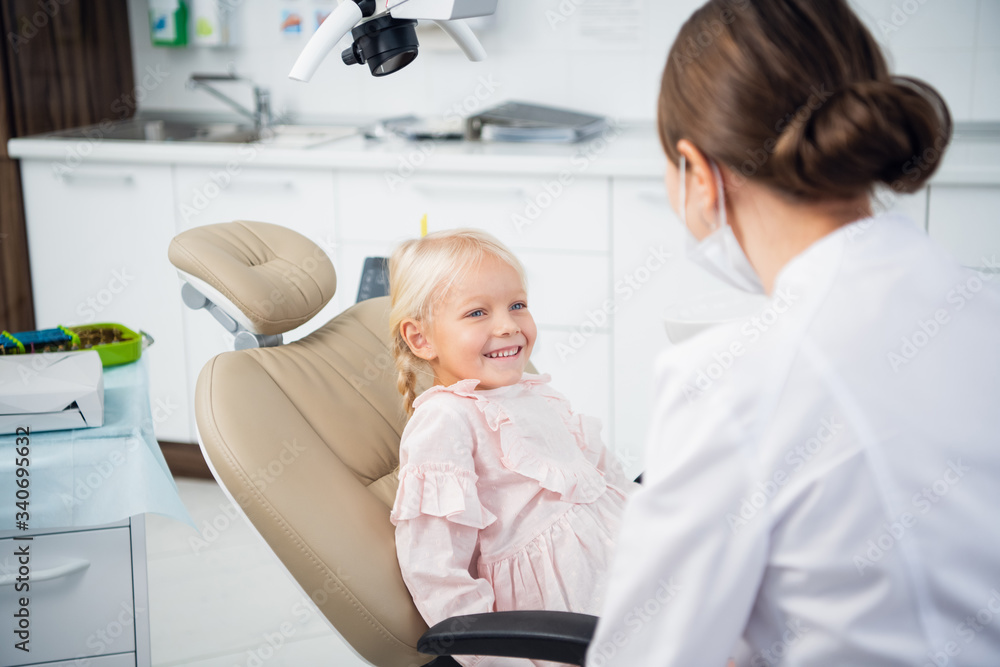 A little happy girl sitting in the dentist's chair and smiling at the doctor A little happy girl sitting in the dentist's chair and smiling at the doctor