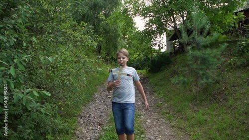 White kid walking along cuntryside rural road going to play wooden boomerang outdoors. Boy walks to throw boomerang. photo