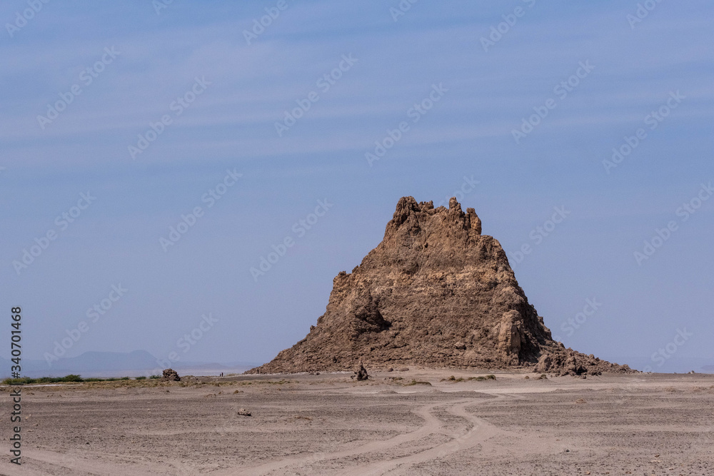 Two children walking next to a rock formation in lake Abbe salt desert