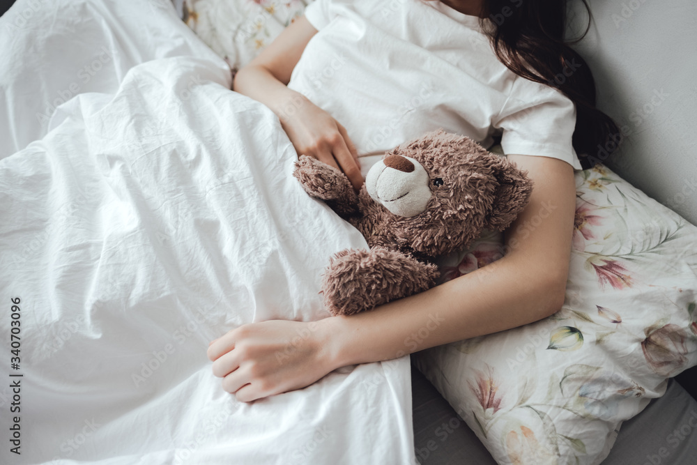 The girl lies in bed under a blanket with a teddy bear at home. The girl lies in bed under a blanket with a teddy bear at home.