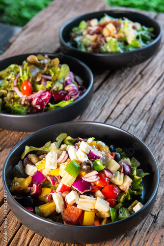 Greek salad, Japanese salad, Caesar salad, in a black ceramic bowl, on a wooden table, for health lovers, vegetable lovers.