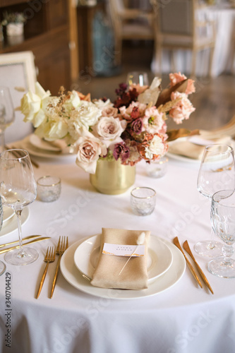 Luxury cozy autumn wedding table decoration in the restaurant. Fresh and dried flowers  roses  carnations. Beautiful table setting  golden appliances  fork and knife  calligraphy guest seating card.