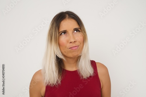 Gloomy, wondering young woman looking up with lips together, being upset thinking about something important, keeps hands down.