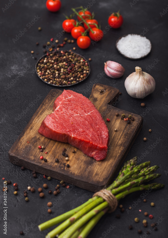 Slice of Raw Beef sirlion steak on wooden chopping board with tomatoes,garlic and asparagus tips. Slice of Raw Beef sirlion steak on wooden chopping board with tomatoes,garlic and asparagus tips.