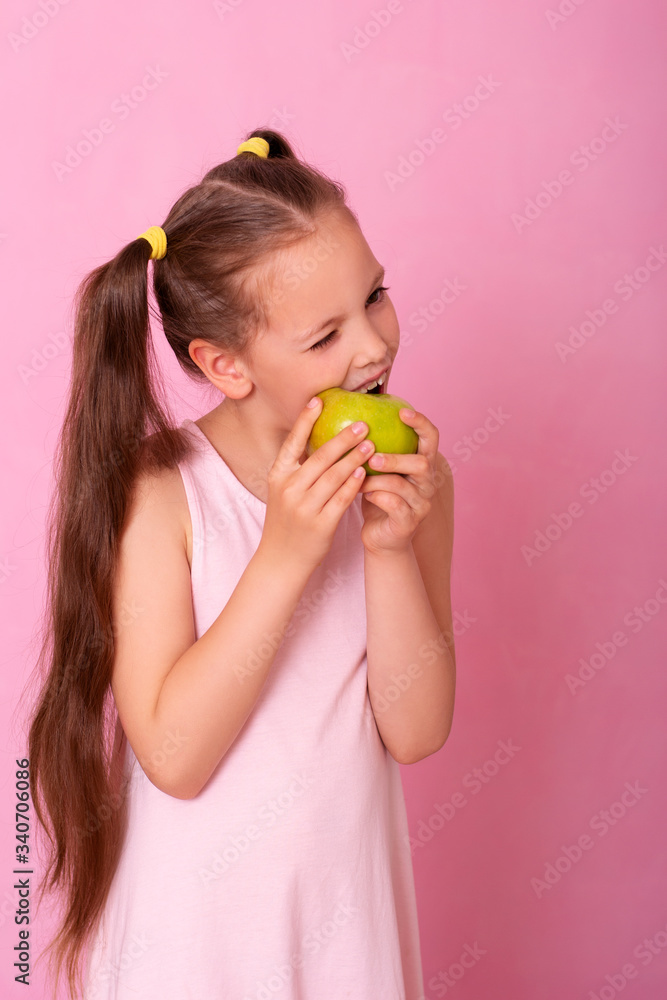 A beautiful girl standing on a pink background holding green apple in her hand and biting. A beautiful girl standing on a pink background holding green apple in her hand and biting.