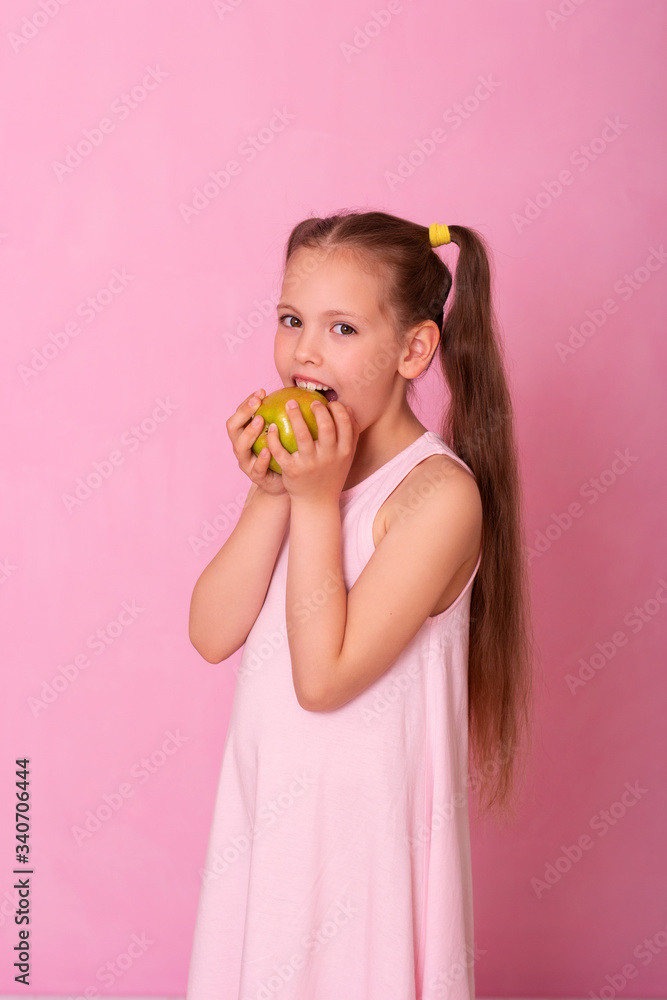 6 year old girl on pink background eats a green apple and smiles. 6 year old girl on pink background eats a green apple and smiles.