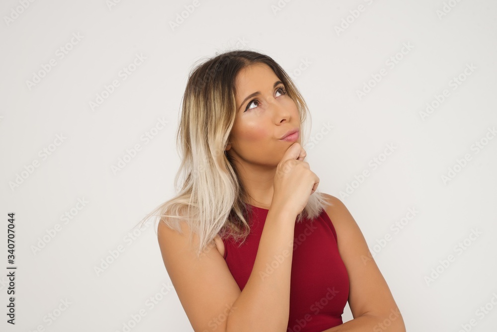 Portrait of thoughtful smiling girl keeps hand under chin, looks sideways, thinking or wondering about something with interest, dressed casually, poses against gray studio. Taking decisions concept. Portrait of thoughtful smiling girl keeps hand under chin, looks sideways, thinking or wondering about something with interest, dressed casually, poses against gray studio. Taking decisions concept.