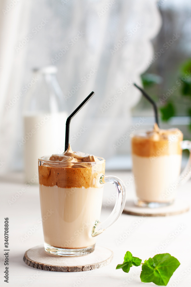 Dalgona coffee based on instant coffee, sugar, hot water and milk in glass cups with a cocktail tube on a wooden saw cut, against the background of the window. Vertical orientation Dalgona coffee based on instant coffee, sugar, hot water and milk in glass cups with a cocktail tube on a wooden saw cut, against the background of the window. Vertical orientation
