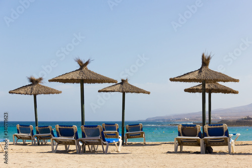 Wicker sun umbrellas with blue hammocks on empty beach in Fuerteventura. Nobody on sunny day in Caleta de Fuste, Canary Islands. Summer holidays, tourism crisis concepts © Josu Ozkaritz
