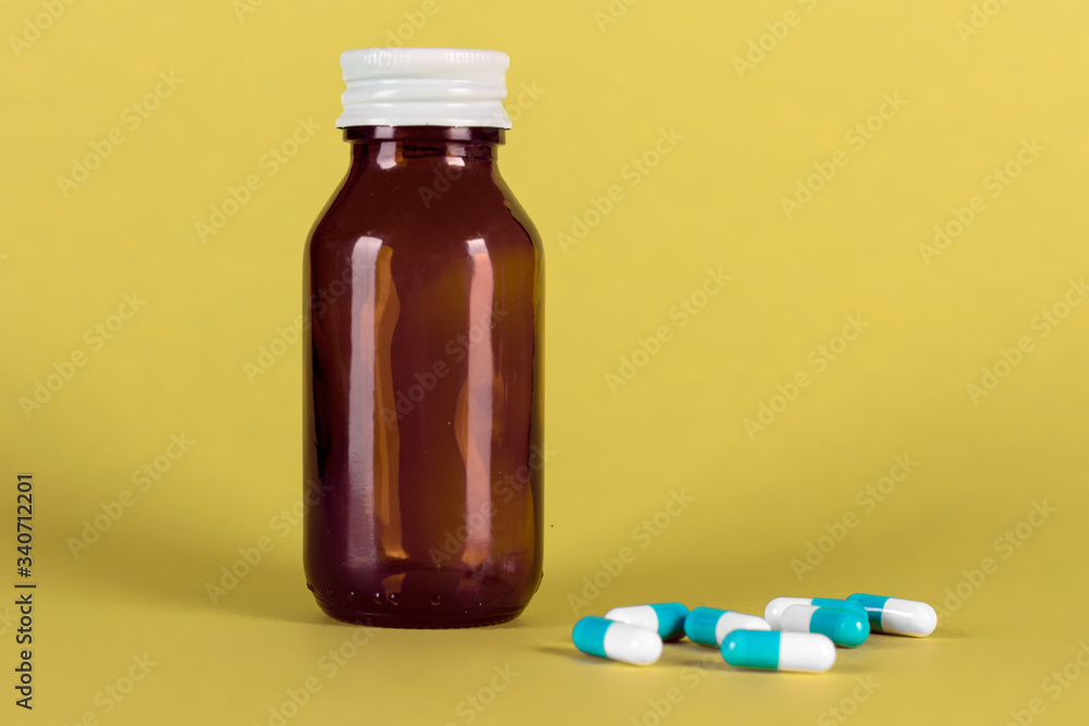 Big medicine glass bottle with blue medicines, cap on and yellow background Big medicine glass bottle with blue medicines, cap on and yellow background