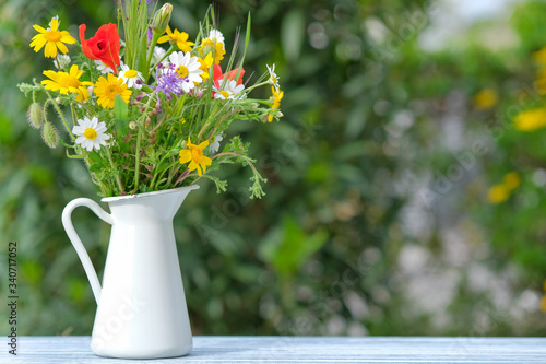Wild flower bouquet in white metallic jug. Still life with bouquet of spring colorful wildflowers against natural green background with copy space. Spring or summer sunny day. Morning in a village.