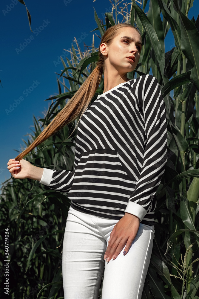 Portrait of a fair-haired girl in fashionable and stylish clothes, among the foliage of a corn field. Portrait of a fair-haired girl in fashionable and stylish clothes, among the foliage of a corn field.