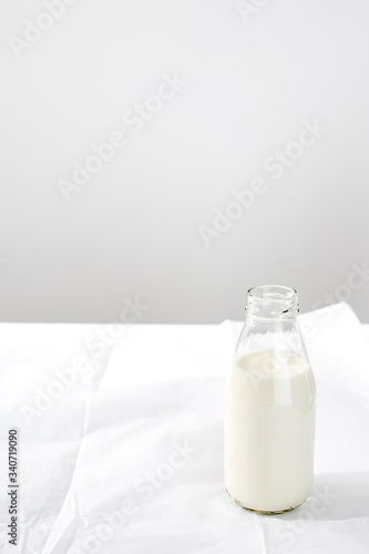 An open bottle of milk is on white crumpled craft paper on the table against the background