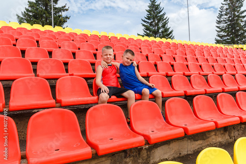 children in sports uniforms sit on red seats on the sports stand of the stadium. fans.