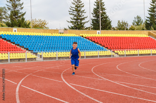boy in sports uniform runs through sports stadium in summer