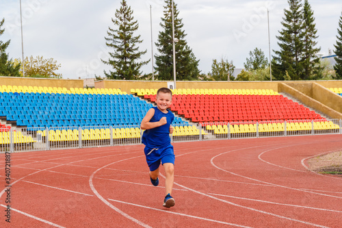 Six-year-old boy in sports uniform runs through sports stadium in summer