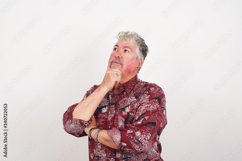 Portrait of thoughtful smiling man keeps hand under chin, looks sideways, thinking or wondering about something with interest, dressed casually, poses against gray studio. Taking decisions concept. Portrait of thoughtful smiling man keeps hand under chin, looks sideways, thinking or wondering about something with interest, dressed casually, poses against gray studio. Taking decisions concept.