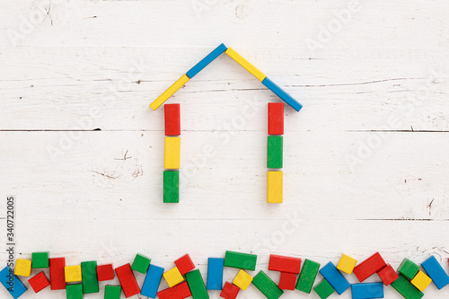 Top view on wooden colorful bricks on a white wooden background. Different-colored wooden blocks are assembled in the shape of a house. School, education and learning concept.