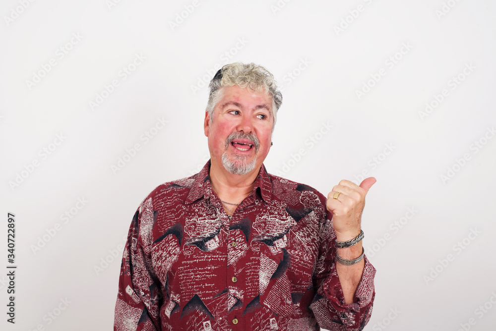 Omg concept. Stupefied caucasian male with surprised expression, opens eyes and mouth widely, points aside with thumb, shows something strange on gray background. Advertisement concept. Omg concept. Stupefied caucasian male with surprised expression, opens eyes and mouth widely, points aside with thumb, shows something strange on gray background. Advertisement concept.