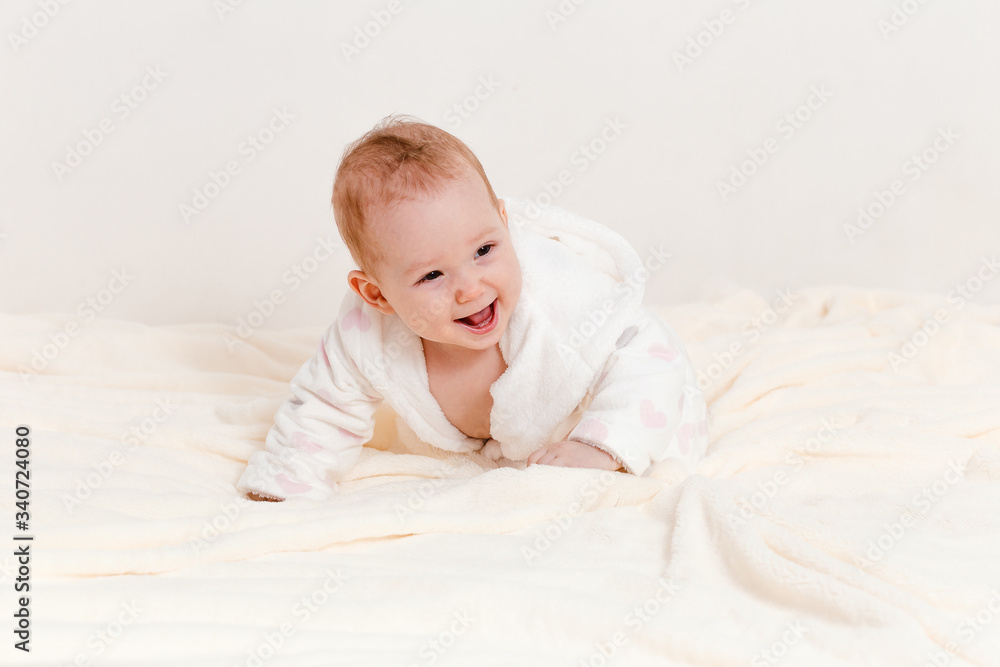 a cheerful baby girl in a Terry robe and a diaper crawls on the bed after bathing