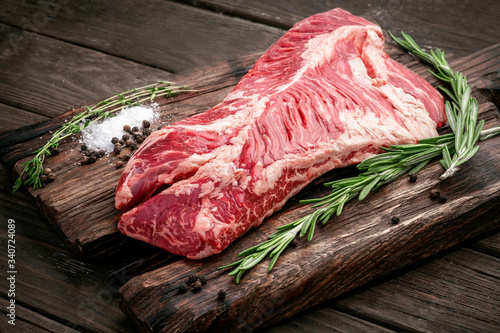 Raw hanging tender or onglet steak of beef on wooden Board with rosemary and thyme on wooden background photo