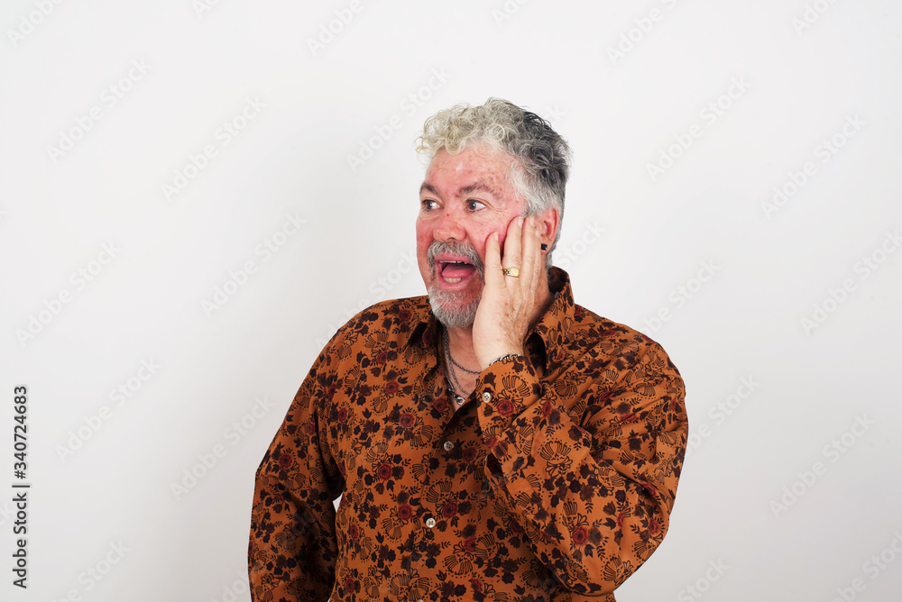 Amazement - man excited looking to the side hand on face. Surprised happy young man looking sideways in excitement. Caucasian male model on gray background. Amazement - man excited looking to the side hand on face. Surprised happy young man looking sideways in excitement. Caucasian male model on gray background.