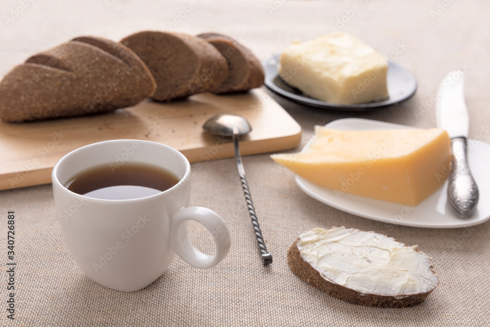 Sliced bread and knife on a cutting board. Butter, cheese, a cup of coffee on a sackcloth. Side view breakfast brunch on table concept Sliced bread and knife on a cutting board. Butter, cheese, a cup of coffee on a sackcloth. Side view breakfast brunch on table concept