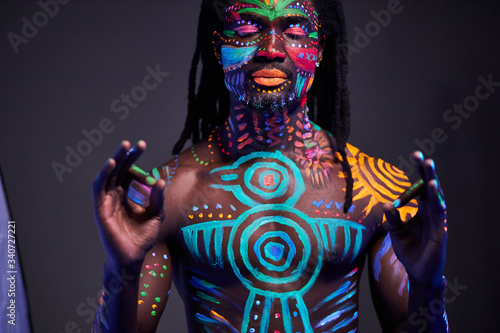 tranquil african man with fluorescent body art practice meditation, show keep calm gesture at camera. yoga, calmness, luminescence, fluorescence concept