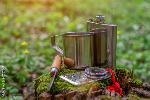Cup of tea on a log in the forest, with forest flowers. Travel Concept.Tourist steel cup and compass in the summer forest.knife on a nature background,