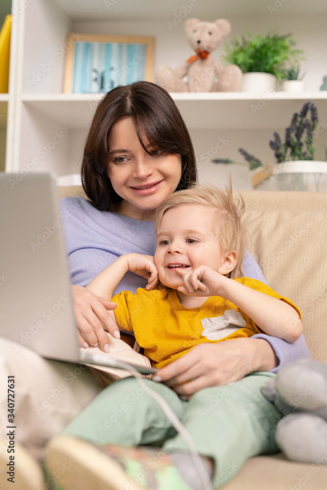 Young cheerful female and her cute little son watching online cartoon at home Young cheerful female and her cute little son watching online cartoon at home