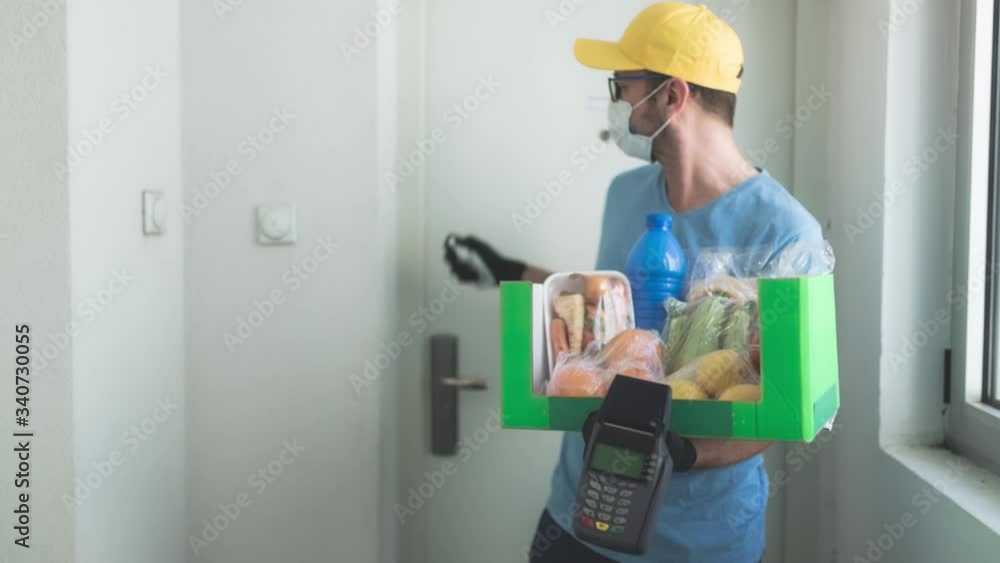 Delivery guy with protective mask holding box / bag with groceries and POS for contactless payment. Delivery guy with protective mask holding box / bag with groceries and POS for contactless payment.