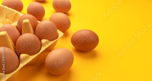 Brown chicken eggs in cardboard box on yellow background