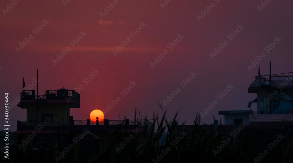 Obraz premium Silhouetted little girl playing on the terrace against the setting sun. People are not allowed to go out due to recent lockdown imposed amid concerns over coronavirus outbreak. selective focus