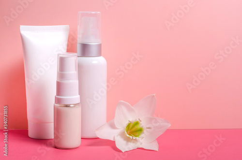 White tubes for cream and cosmetics on a pale pink background with a flower with copy space. For advertising creams and cosmetics.
