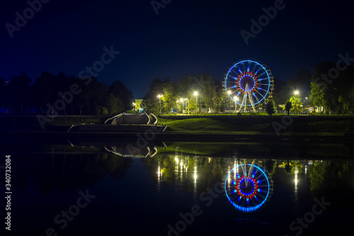 Ferris wheel in a city park on the banks of the river, in which it is reflected in the night.