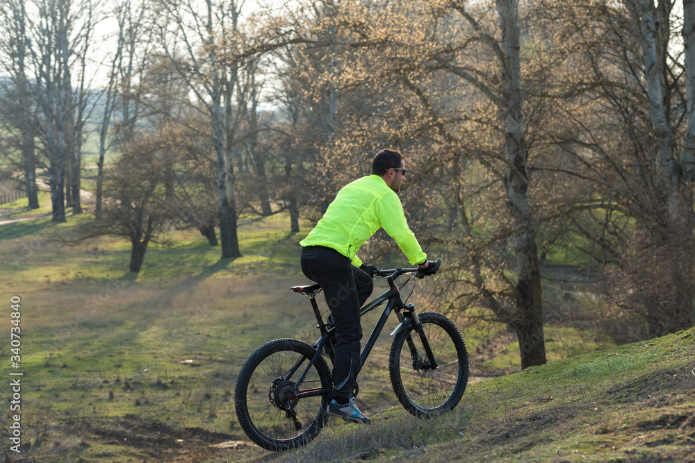 Cyclist in pants and green jacket on a modern carbon hardtail bike with an air suspension fork. The guy on the top of the hill rides a bike. Cyclist in pants and green jacket on a modern carbon hardtail bike with an air suspension fork. The guy on the top of the hill rides a bike.