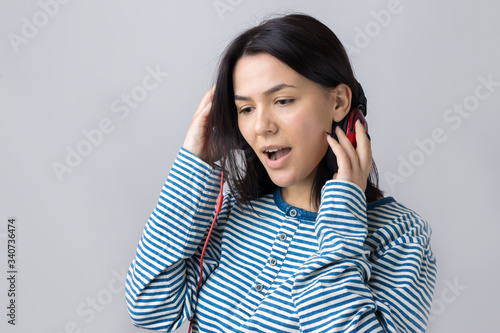 A young girl in a striped vest is listening to music in red headphones in a studio and dancing. © Mountains Hunter