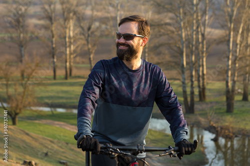 Cyclist in shorts and jersey on a modern carbon hardtail bike with an air suspension fork standing on a cliff against the background of fresh green spring forest © Mountains Hunter