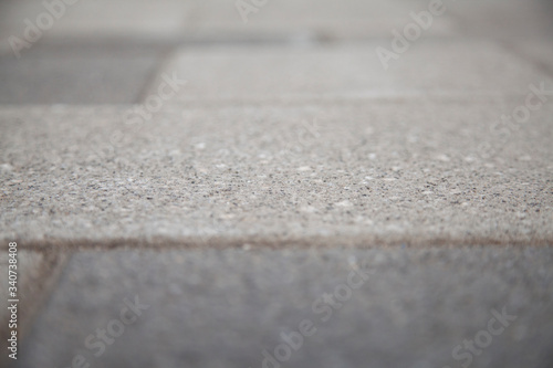 Narrow view of a concrete tile in the blurred sidewalk. Cement block on a pedestrian crossing. Textured abstract background bokeh.