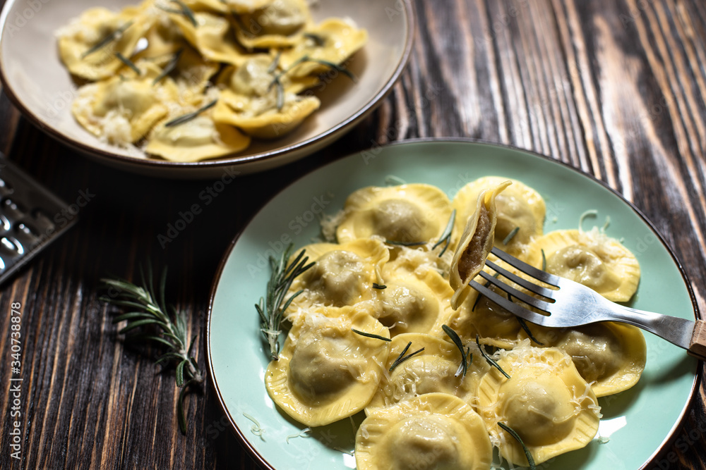 Traditional italian ravioli with rosemary and parmesan served on a rustic wooden table. Italian pasta. Close-up, Ravioli on a fork Traditional italian ravioli with rosemary and parmesan served on a rustic wooden table. Italian pasta. Close-up, Ravioli on a fork