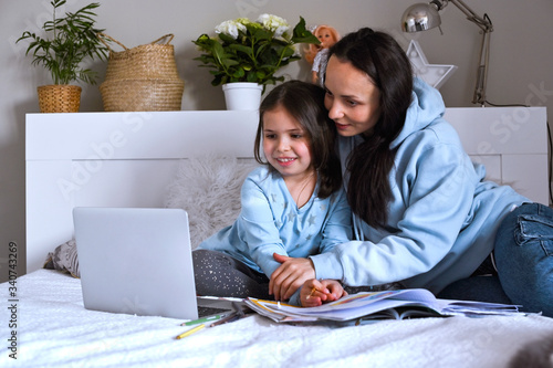 Distance learning online education. Schoolgirl with digital tablet laptop notebook and doing school homework. Mom does homework with her daughter at home in bed. Interactions of children and parents