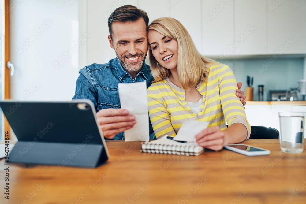 Happy couple managing home finances looking at receipts and tablet Happy couple managing home finances looking at receipts and tablet