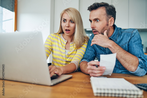 Shocked couple looking at laptop while managing home finances