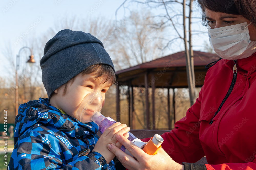 A small boy with illness bronchial asthma getting treatment with aerosol inhaler from his mama outdoors. A small boy with illness bronchial asthma getting treatment with aerosol inhaler from his mama outdoors.