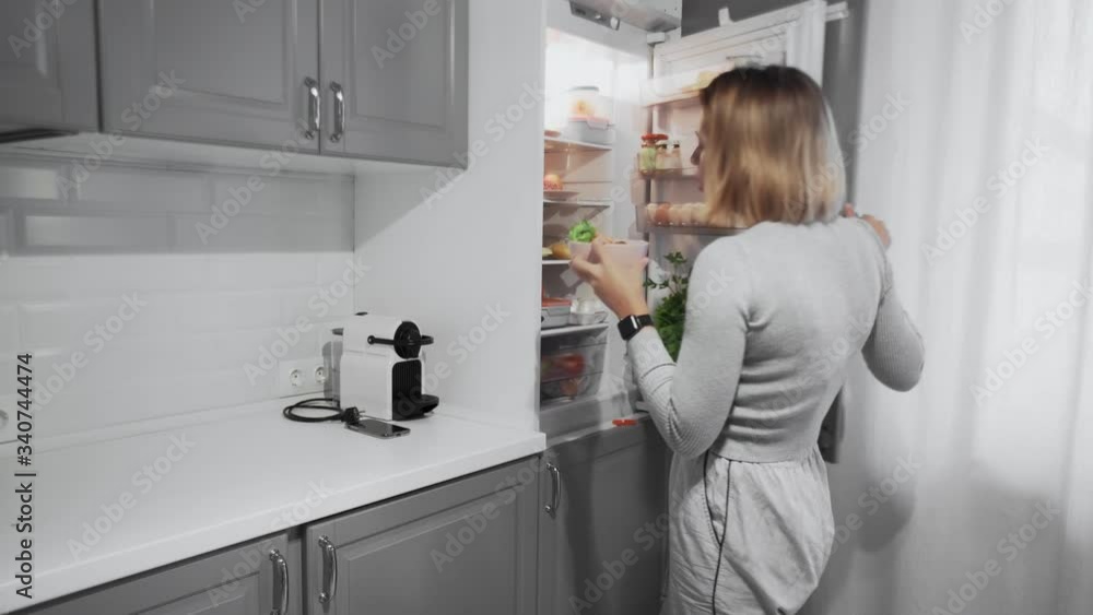 Woman opens refrigerator door in kitchen at home and takes salad Woman opens refrigerator door in kitchen at home and takes salad